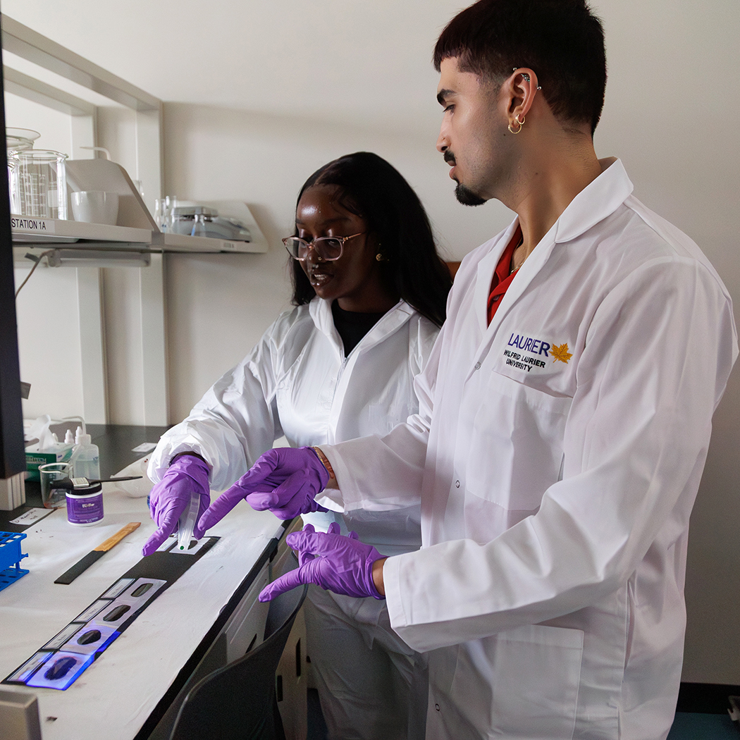 Two student participants use a spray bottle to coat evidence in luminol