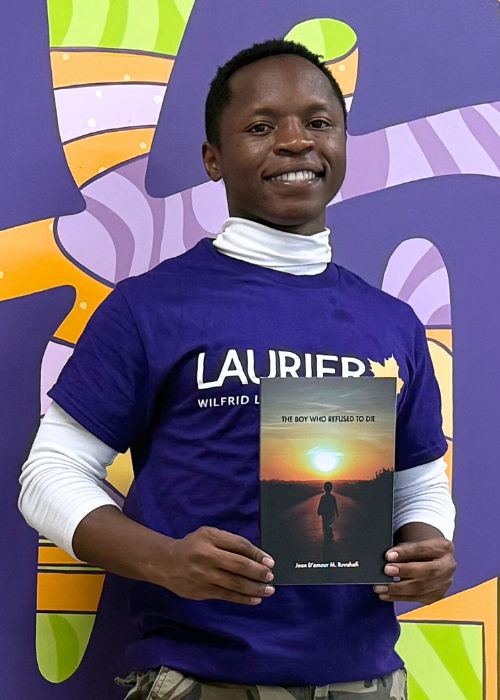 Jean D'amour Ruvahafi stands with his book titled The Boy Who Resufed to Die.