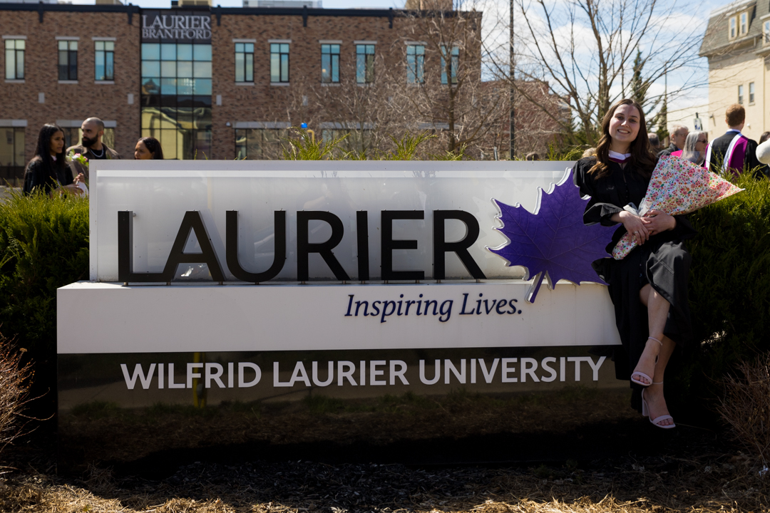 graduate poses in front of Laurier sign